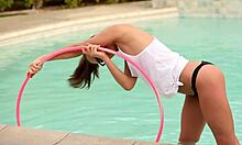 Petite amie à la queue de cheval portant des lunettes pose avec un cerceau de hula dans la piscine